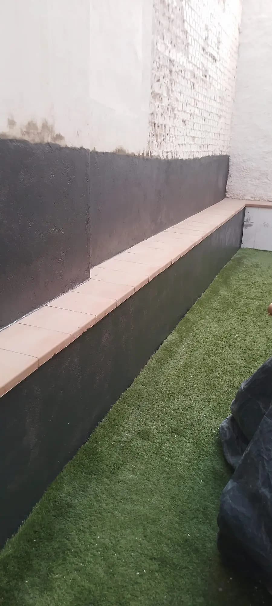 Patio con el muro impermeabilizado en negro y césped artificial